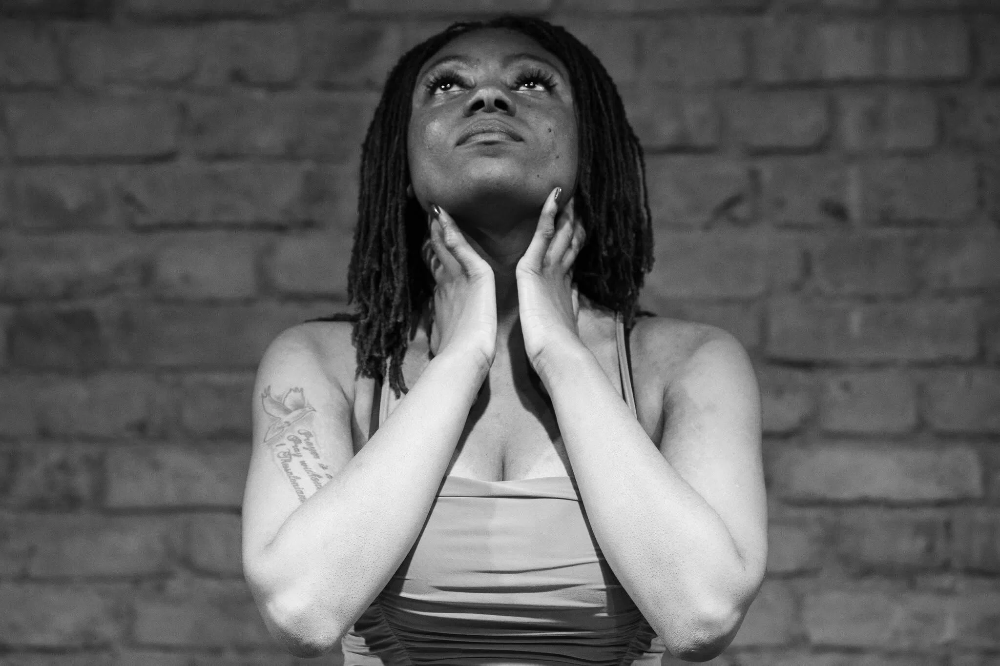 Black-and-white portrait of Tanica looking upward, her hands resting near her face